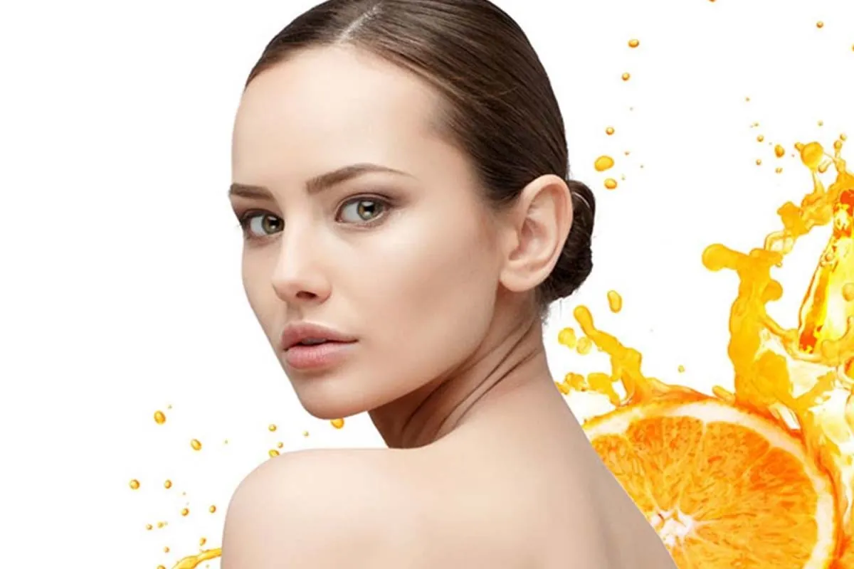 Mujer con piel luminosa junto a naranja y vitamina C