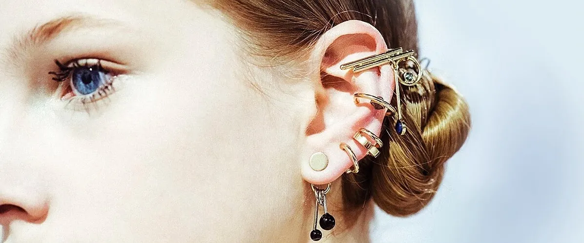Oreja con varios piercings Oreja femenina con múltiples piercings y pendientes dorados decorativos