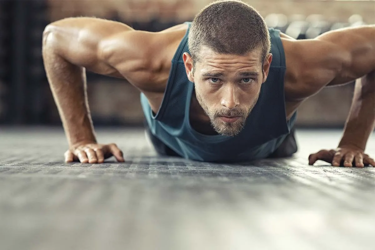 Deporte después de injerto capilar Hombre musculoso haciendo flexiones en gimnasio tras recuperación de injerto capilar
