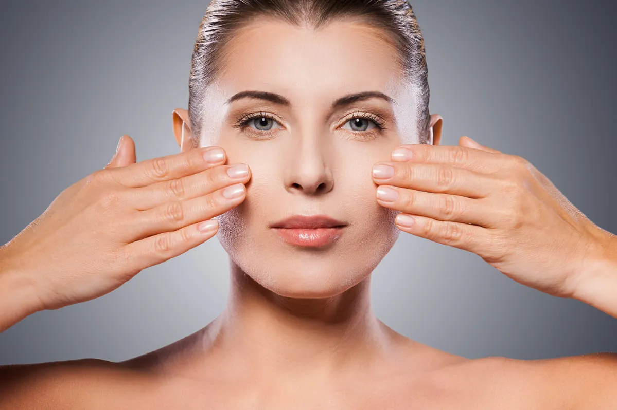 Flacidez facial a los 30 Mujer joven tocando pómulos mostrando firmeza facial a los 30