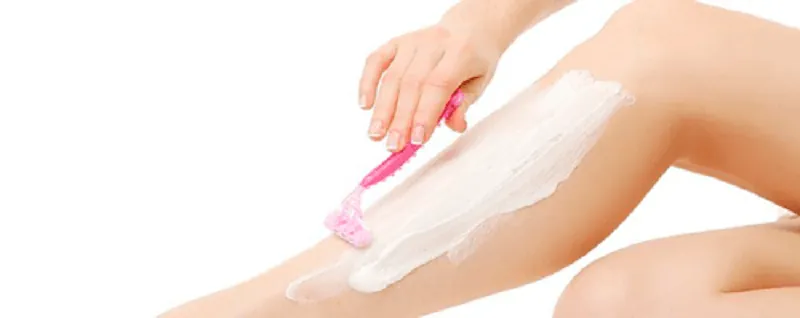 Rasurado previo depilación láser Mujer rasurando su pierna con maquinilla rosa y espuma